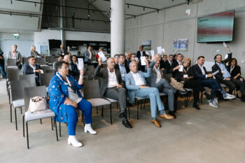 Menschen im Publikum halten einen Folder in die Luft